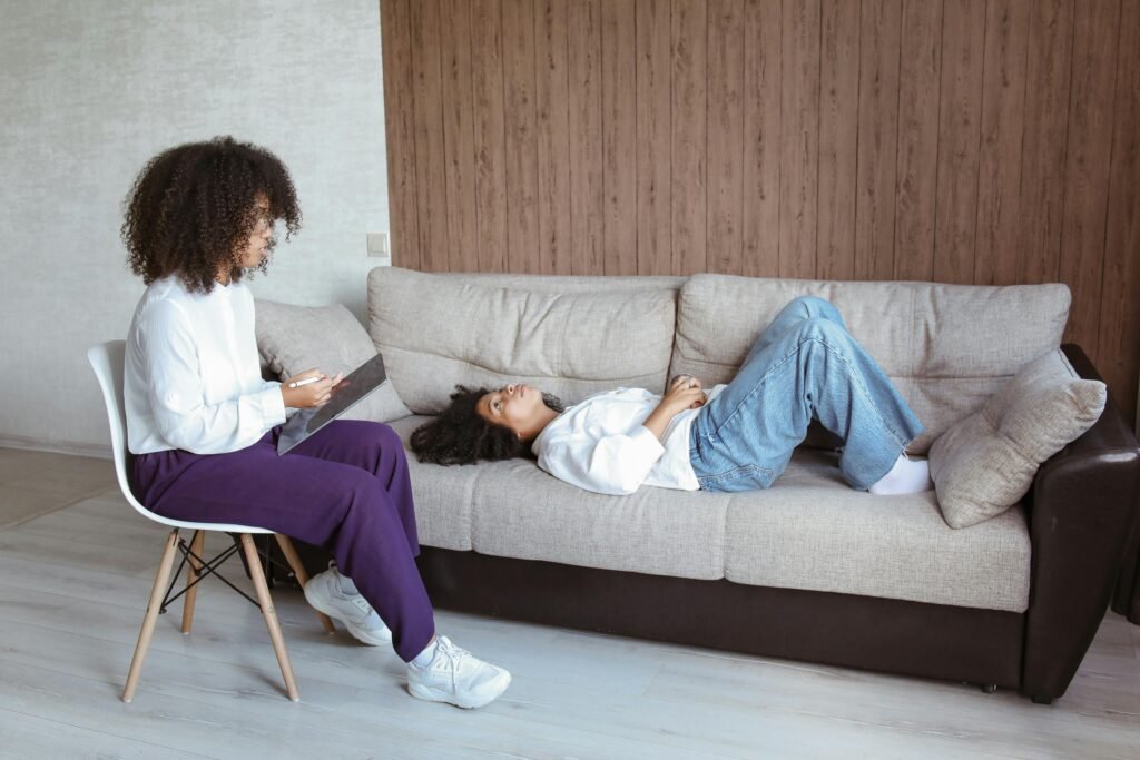 A Woman Lying on the Couch while Looking to the Woman Sitting on the Chair